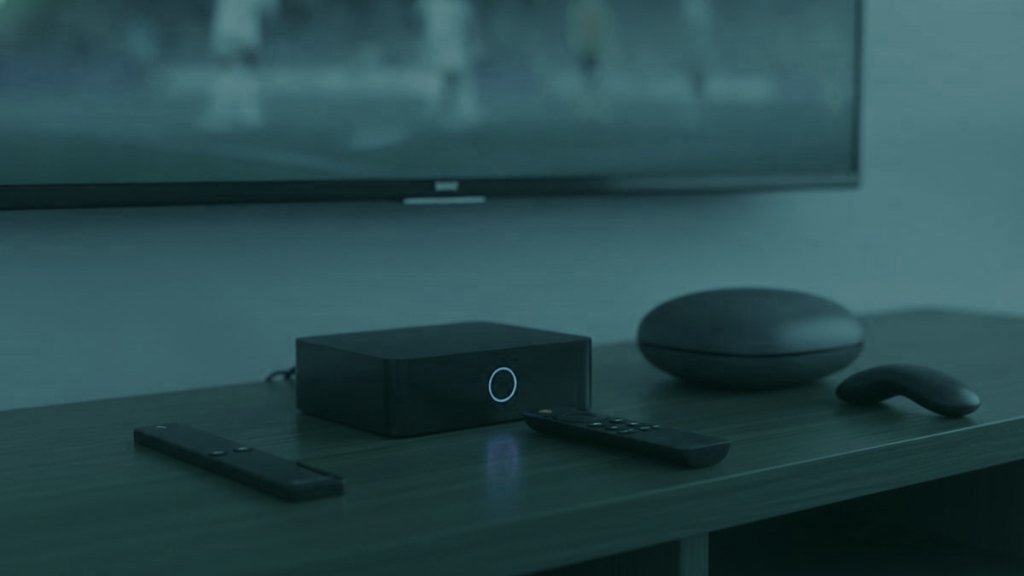 A streaming stick, a set-top box and a round streaming box with their remotes on a TV console