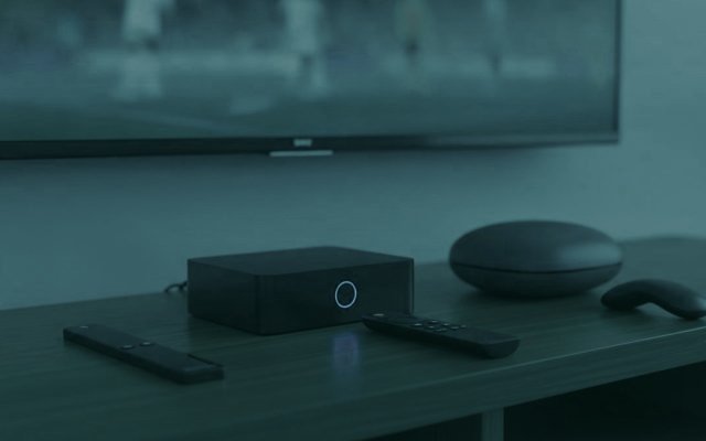 A streaming stick, a set-top box and a round streaming box with their remotes on a TV console